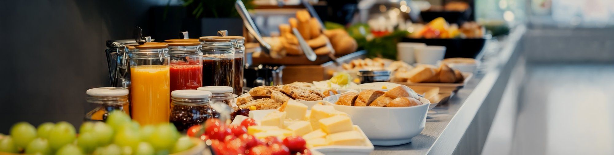 Buffet mit verschiedenen Speisen wie Käse, Obst, Brötchen und Getränken auf einer langen Theke angerichtet